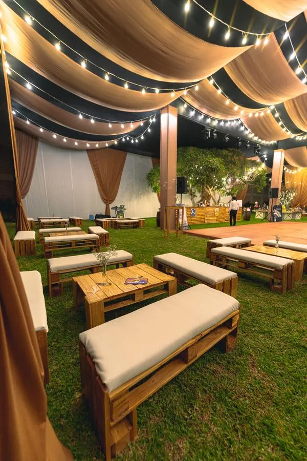 Área lounge con muebles pallet y luces festón en jardín nocturno Cinco Olivos